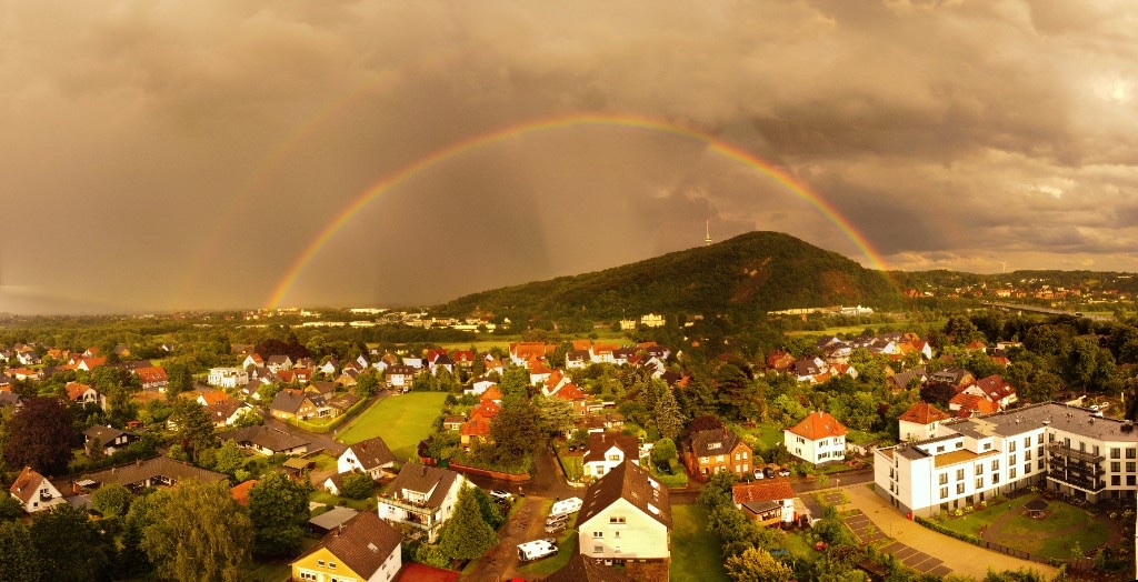 Doppelter Regenbogen über der Stadt und dem begrünten Hügel
